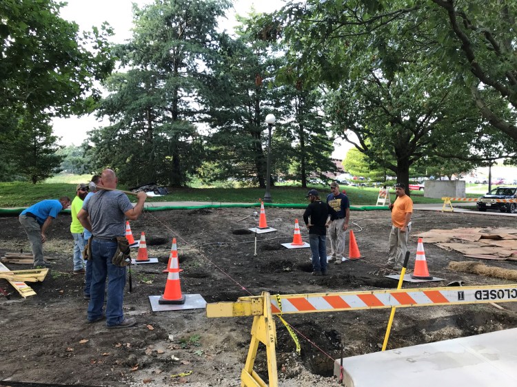 Seven men dressed in workwear in the footprint of the bridge prior to construction.